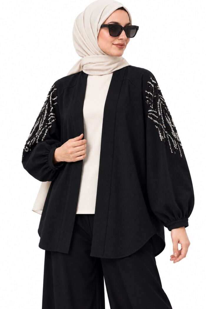 Cardigan long noir à motifs argentés sur les manches, vu de trois quarts sur une mannequin voilée tenant le bord du cardigan