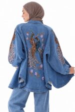 Cardigan long en jean bleu brodé, avec broderies de paons et fleurs, porté par une femme voilée vue de dos